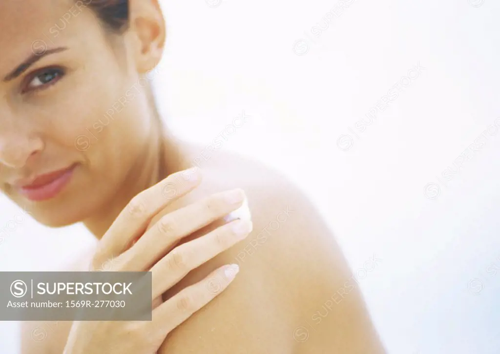 Woman applying sunscreen to shoulder, partial view