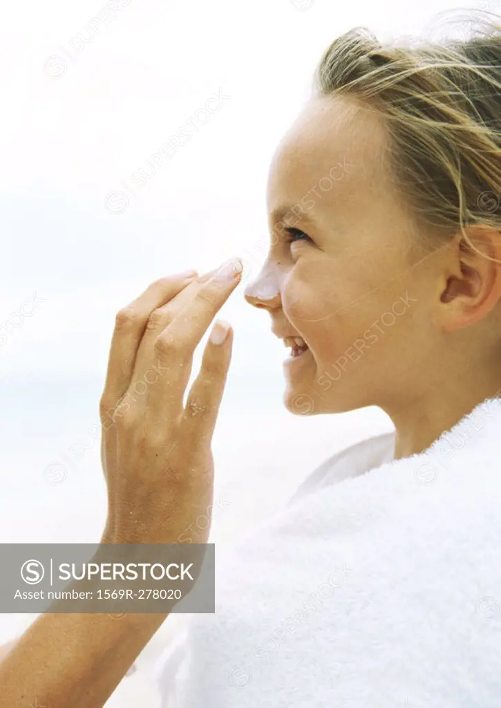 Little girl wrapped in towel having sunscreen rubbed into nose by mother