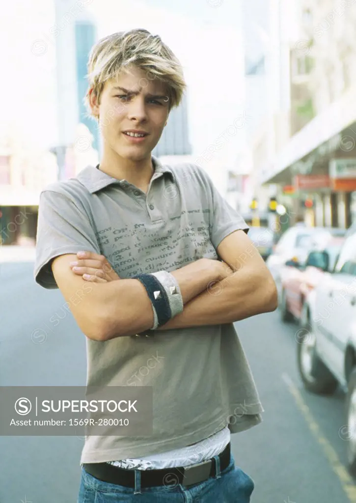 Teenage boy standing in street with arms folded, portrait