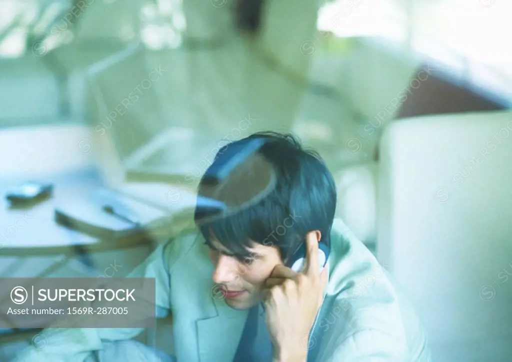 Man using cell phone, seen through glass pane