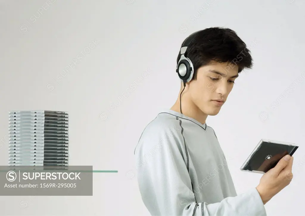 Young man listening to headphones, looking at cd