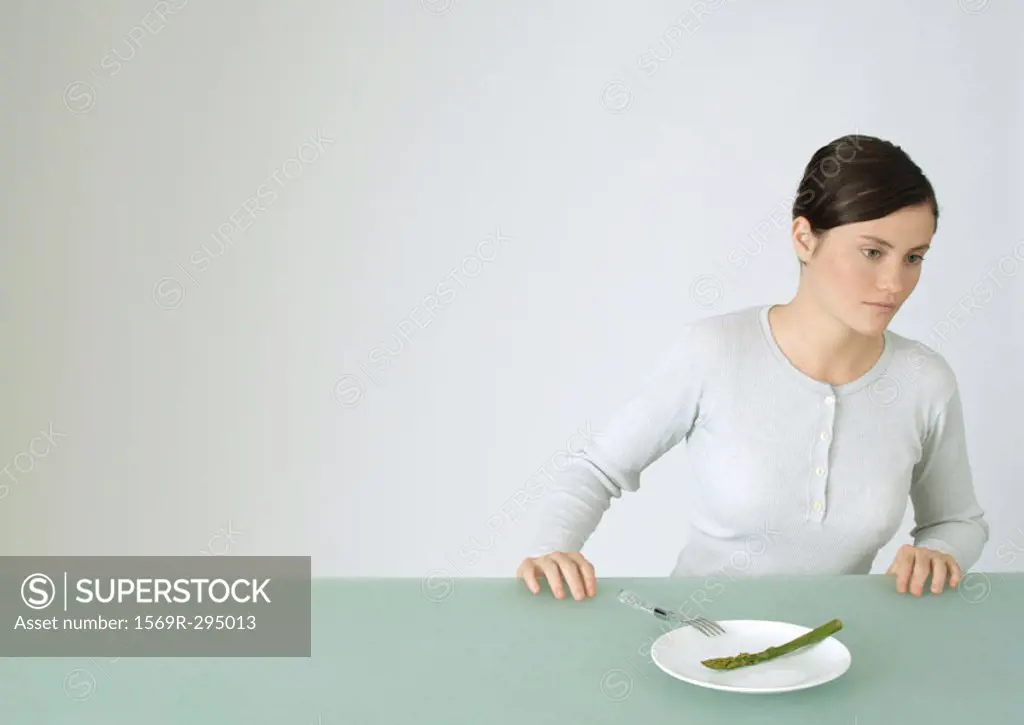 Young woman sitting at table, in front of plate with single asparagus