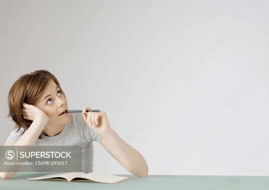 Young woman sitting with open notebook, holding pencil to mouth