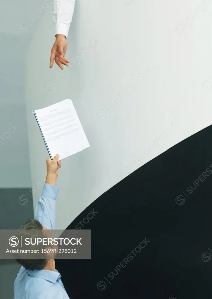 Man holding up document for second person reaching down
