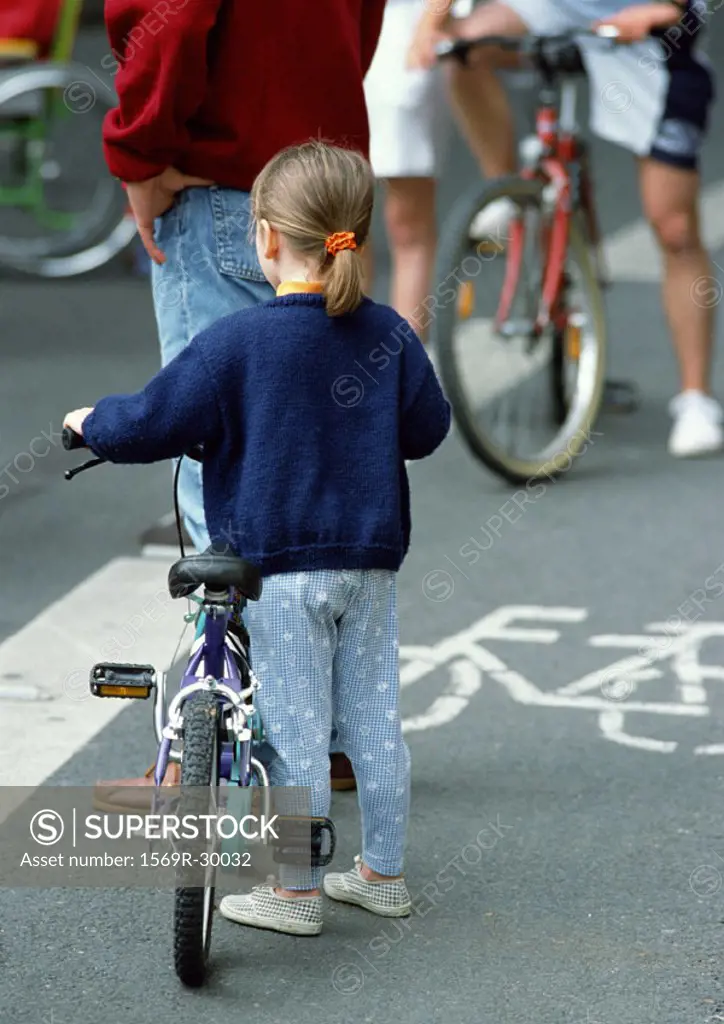 Young girl standing with bike near man and other bikers, view from behind