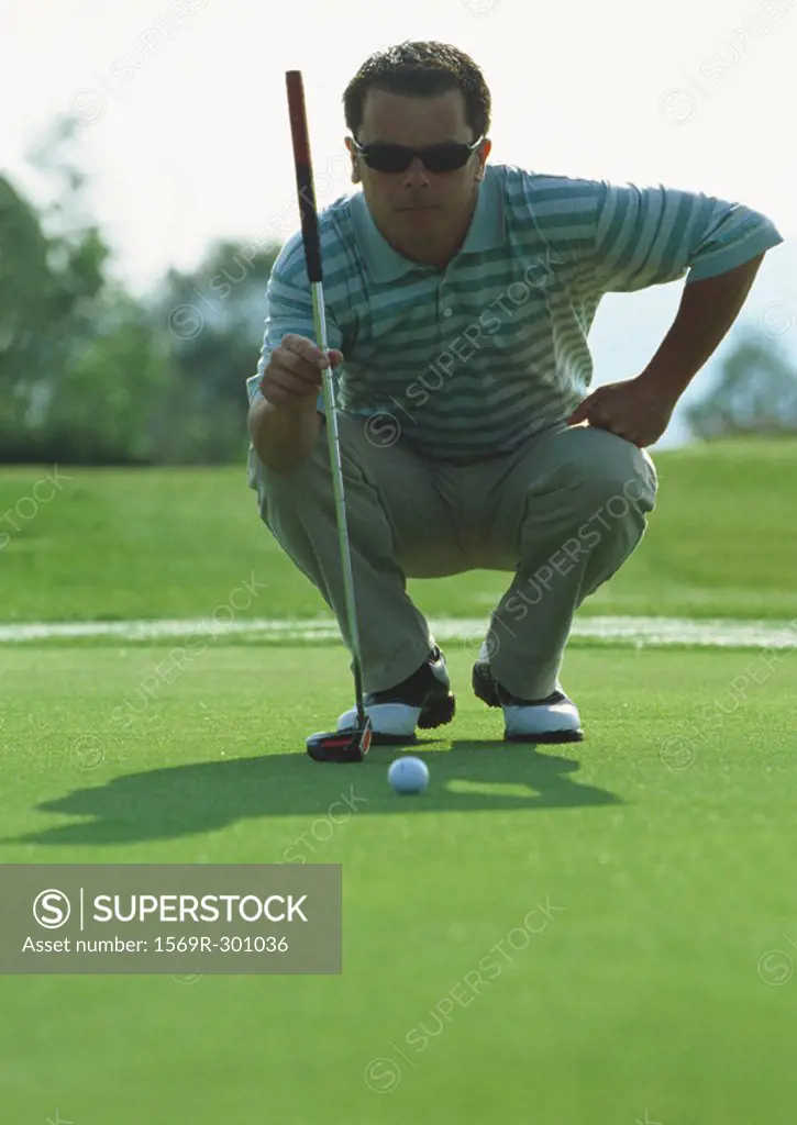 Golfer squatting on green, front view