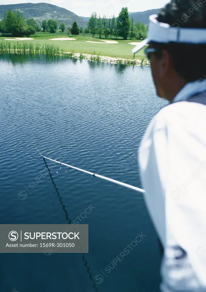Golfer retrieving ball in pond with pole