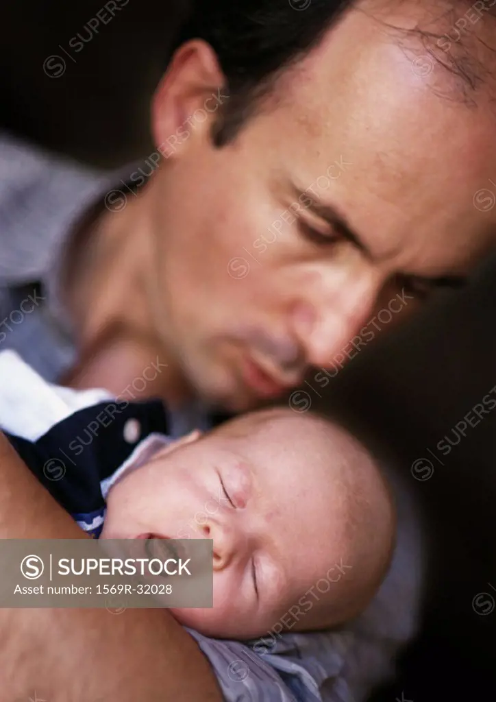 Man holding and looking down at sleeping baby, focus on baby, eyes closed and mouth open, close-up