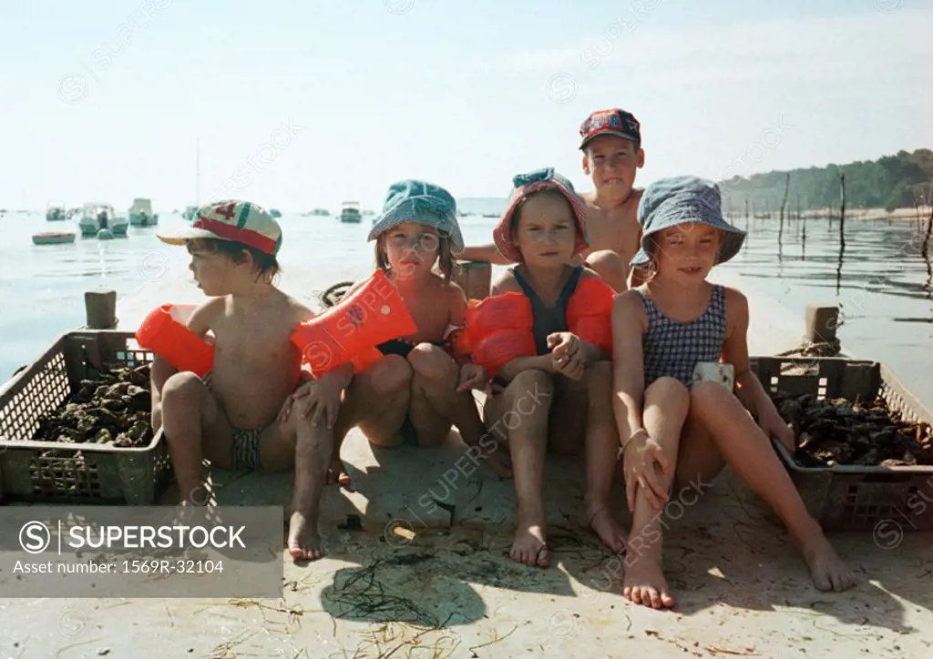 Children sitting lined up, wearing water wings, on beach