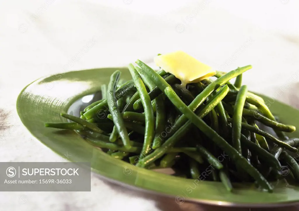 Cooked green beans with pat of butter on top, on green plate, close-up