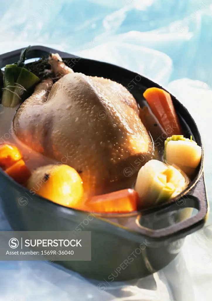 Whole chicken in deep casserole dish with vegetables, close-up