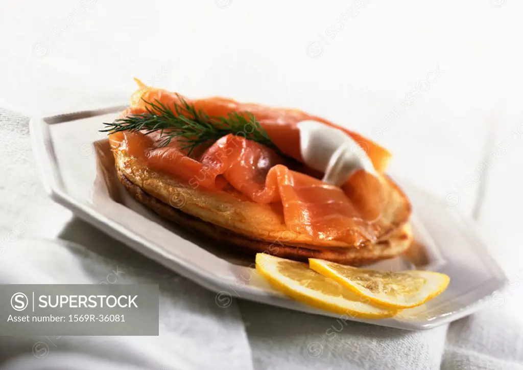 Blinis topped with smoked salmon, herbs and fresh cream, with lemon slices, on plate