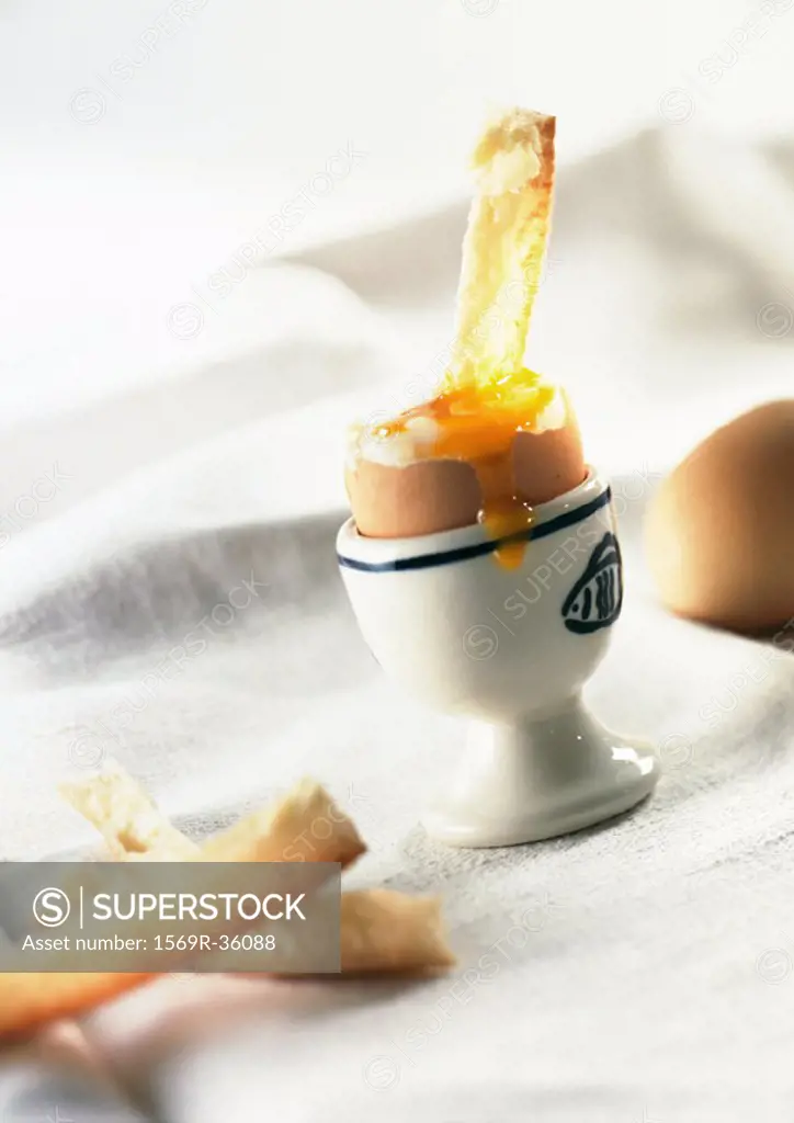 Soft-boiled egg in eggcup with eggyolk dripping over side and bread crusts