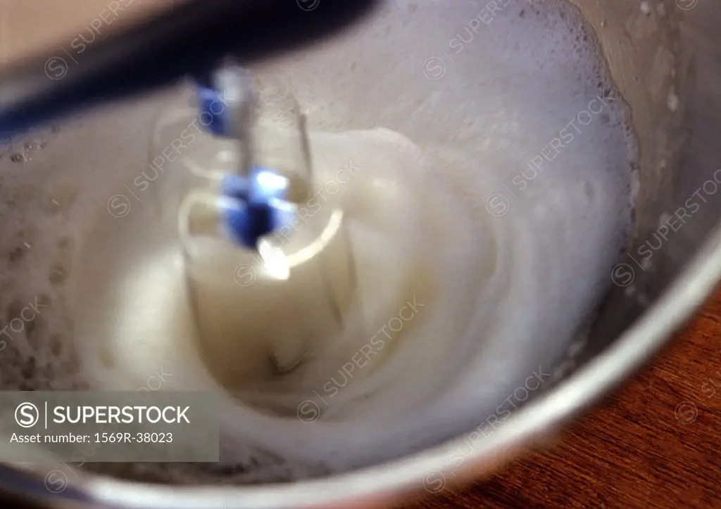 Electric mixer beating egg whites in bowl, close-up