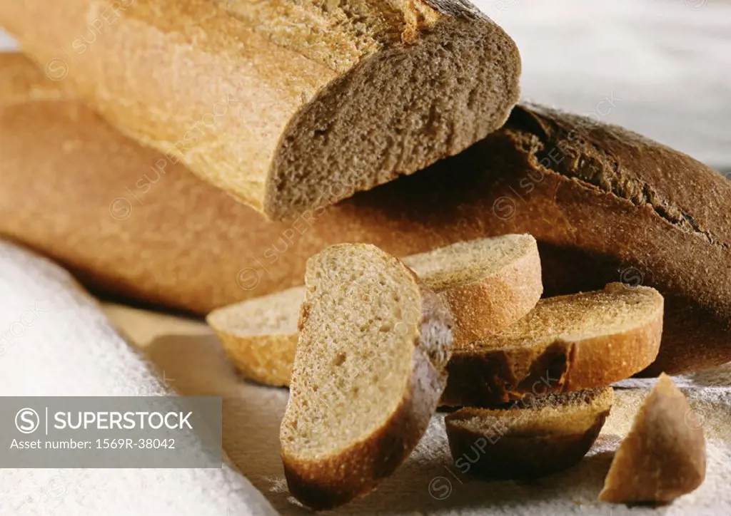 Two loaves of whole wheat bread, one whole, one cut, with slices of bread in a pile, close-up