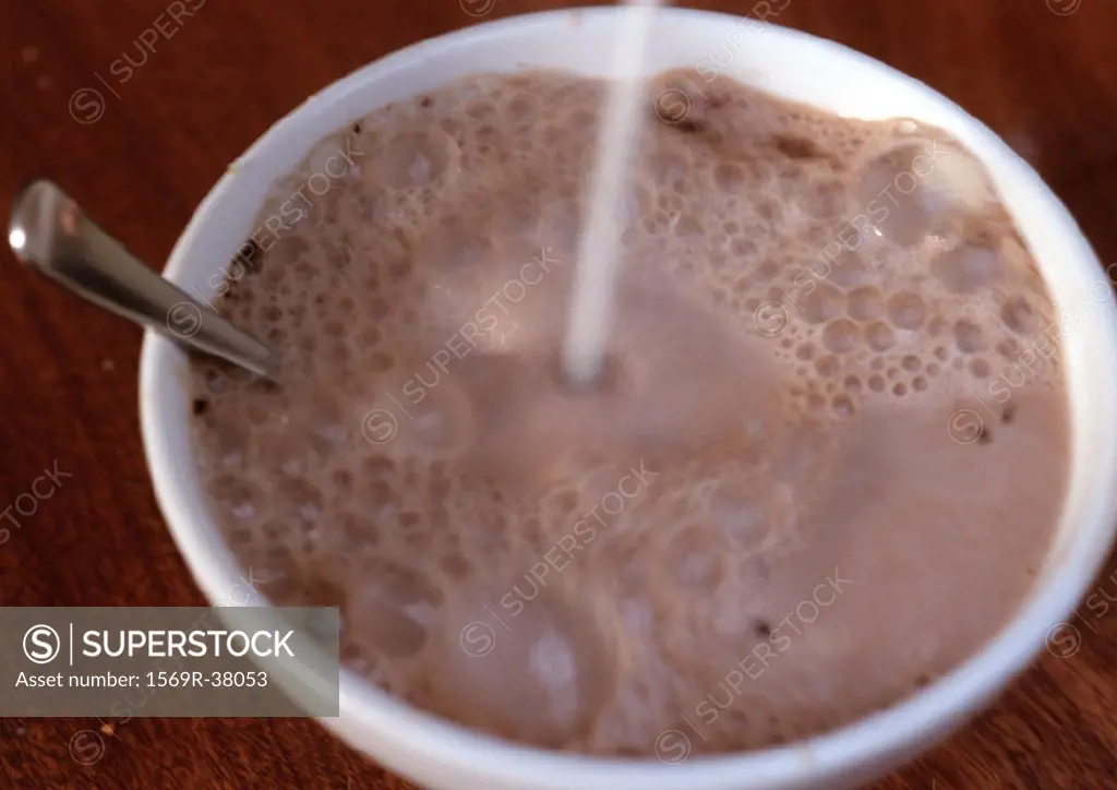 Chocolate milk in bowl, with spoon, liquid being poured into bowl, blurred