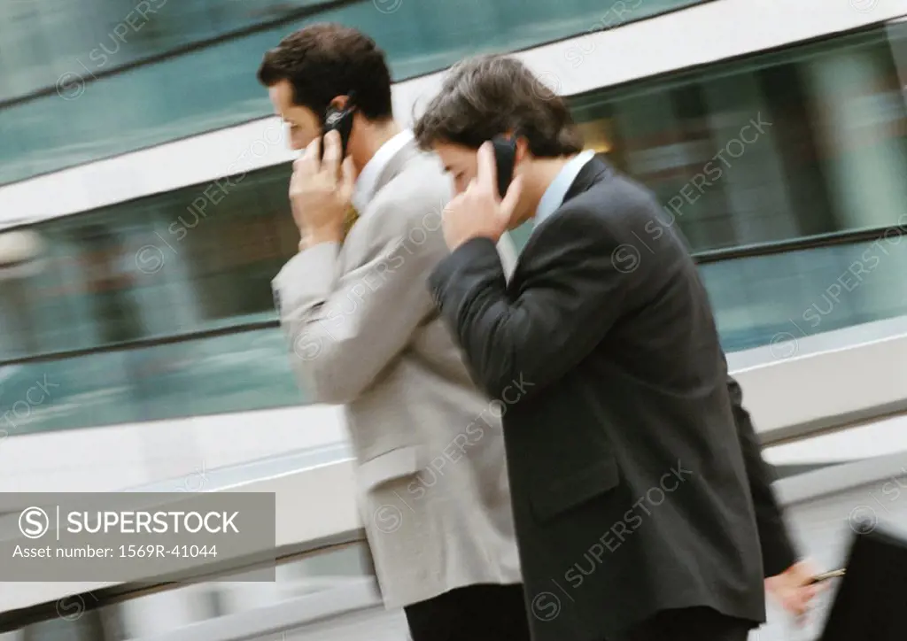 Two businessmen using cell phones outside, side view
