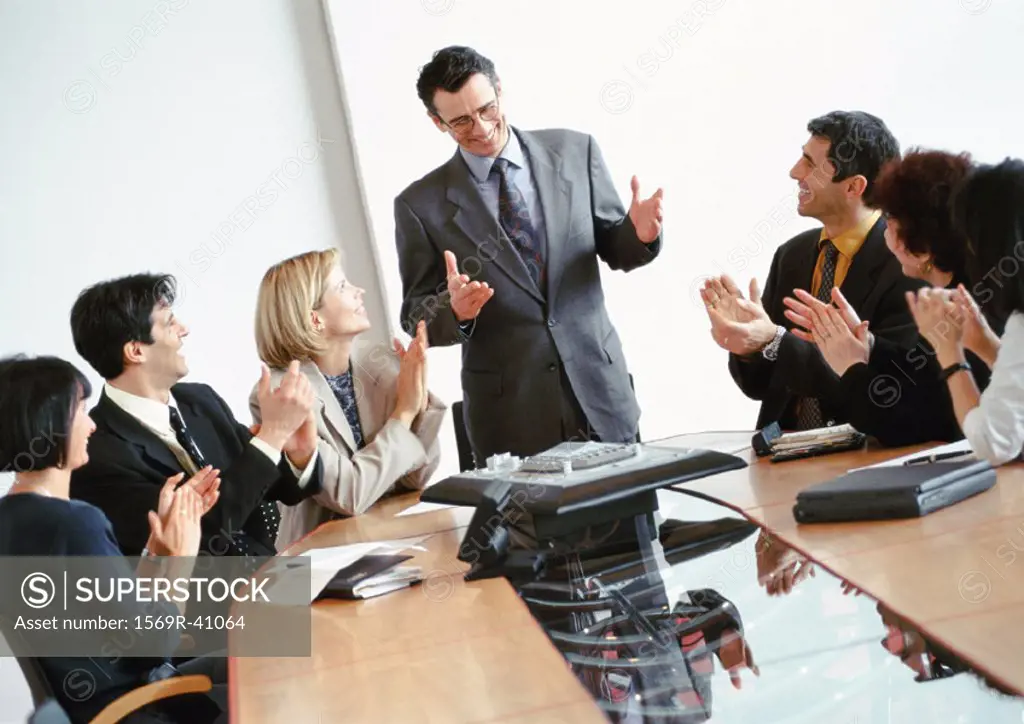 Business people in conference room, applauding businessman standing up