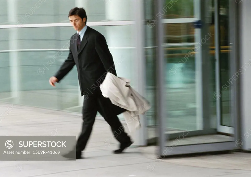 Businessman leaving building, holding overcoat, blurred