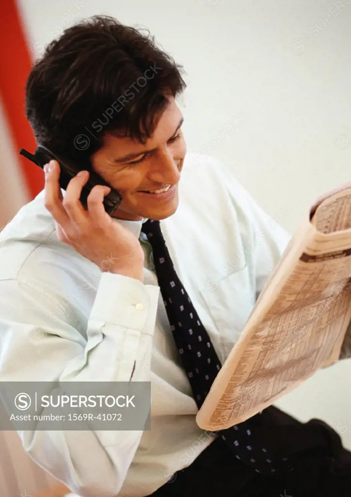 Businessman holding newspaper and cell phone, smiling
