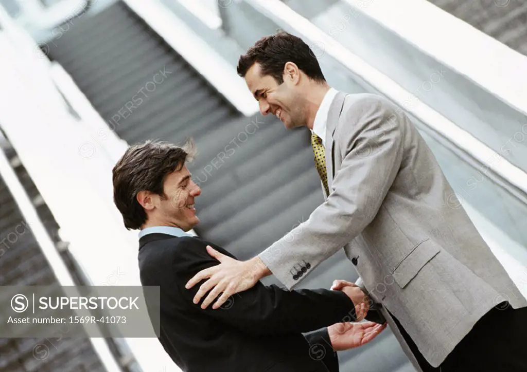 Two businessmen shaking hands in front of stairs