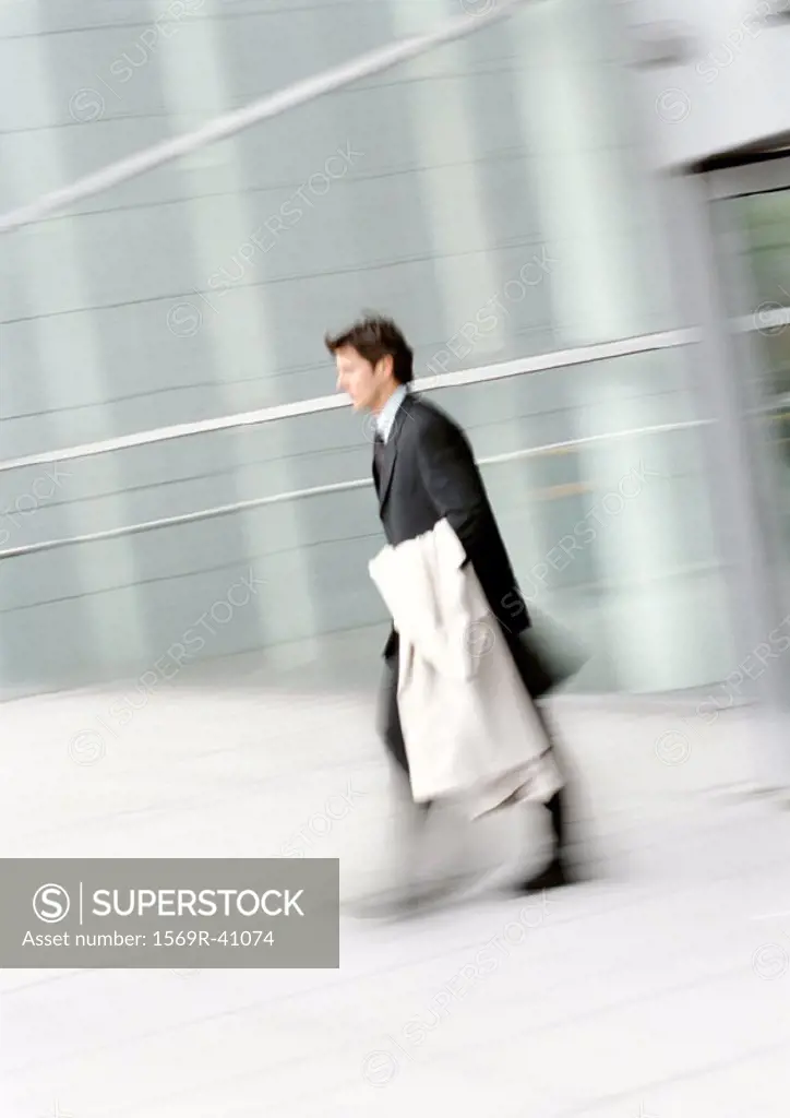 Businessman walking, holding overcoat, blurred