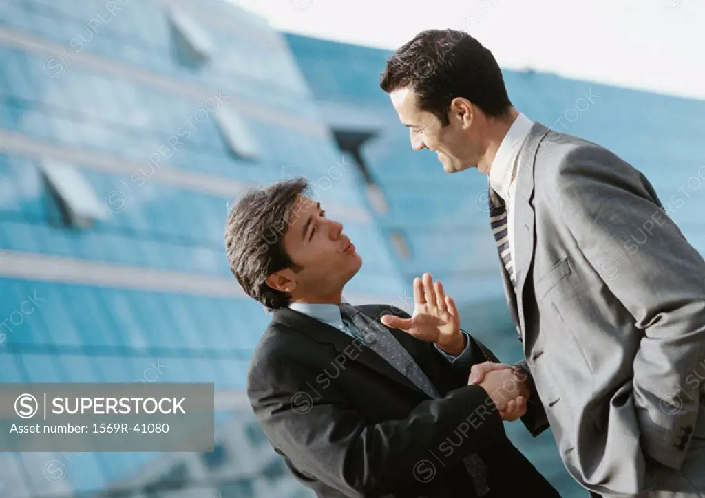Two businessmen shaking hands outside, buildings in background