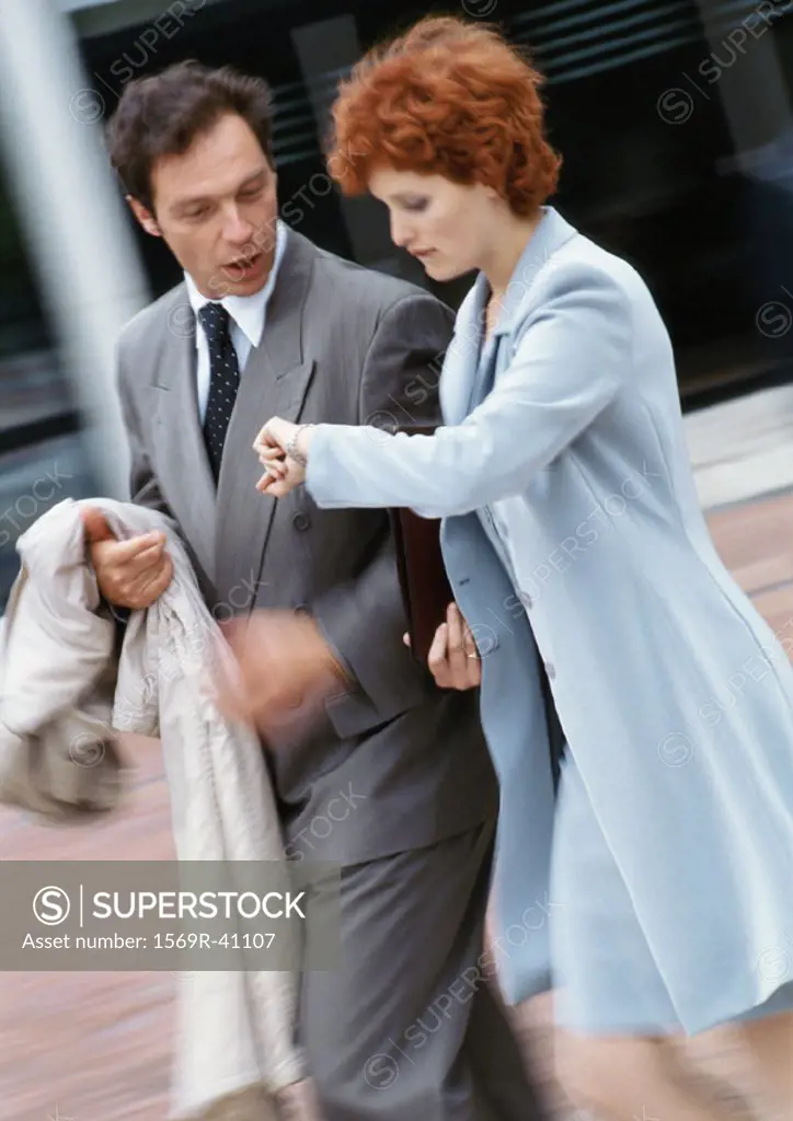 Businessman and businesswoman walking side by side outside, businesswoman looking at watch