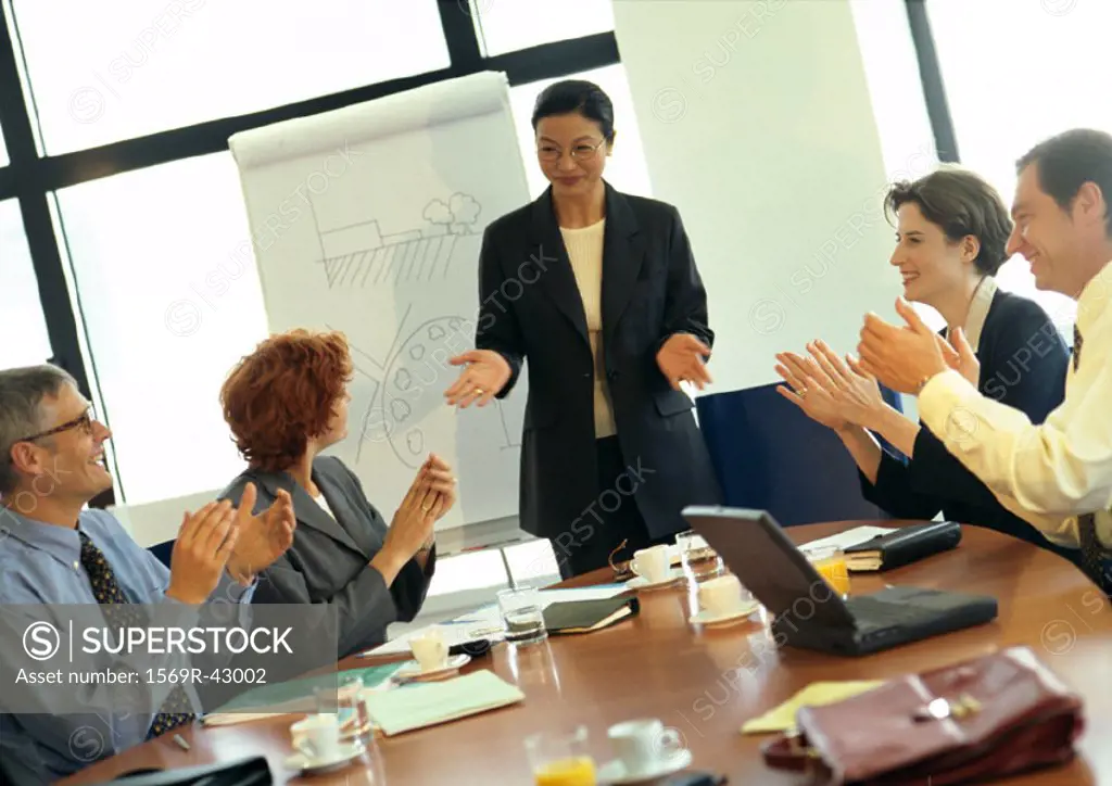 Businesswoman being applauded by colleagues in conference room