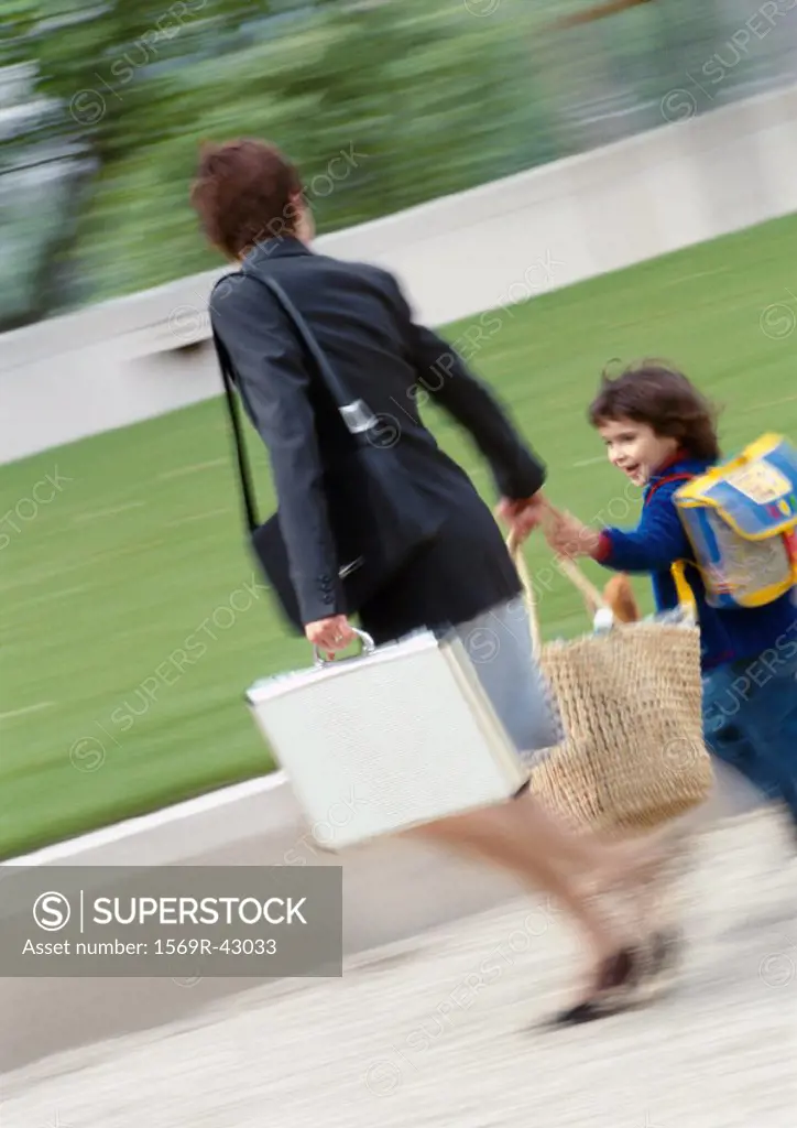 Businesswoman and child outside, walking and holding hands, blurred