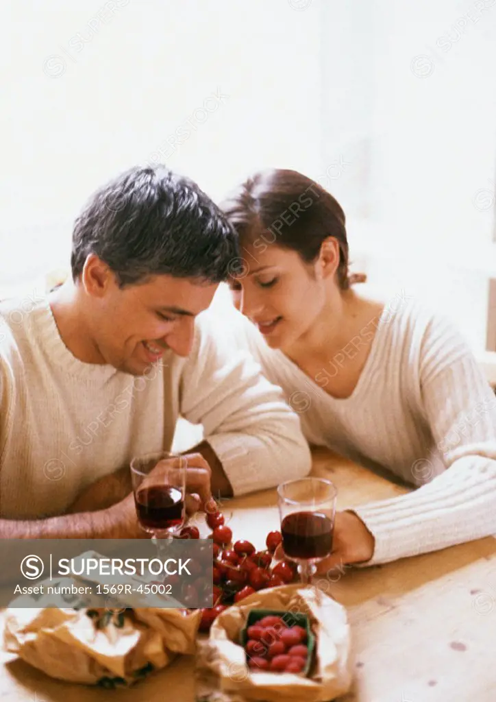 Couple sitting at table, head and shoulders, with berries, cherries, and glasses of red wine