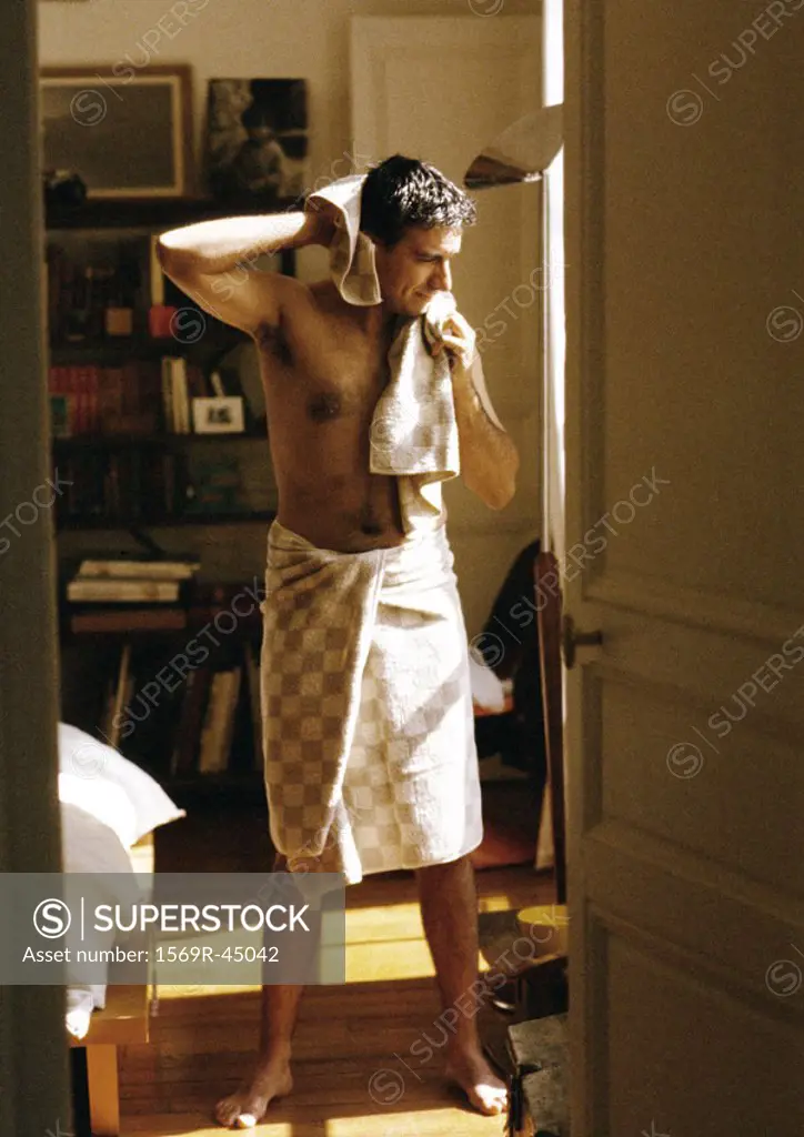 Man with towel wrapped around waist, drying hair with towel, full length
