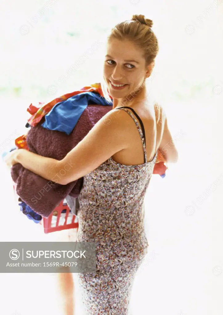 Woman holding laundry basket, looking over shoulder and smiling, rear view
