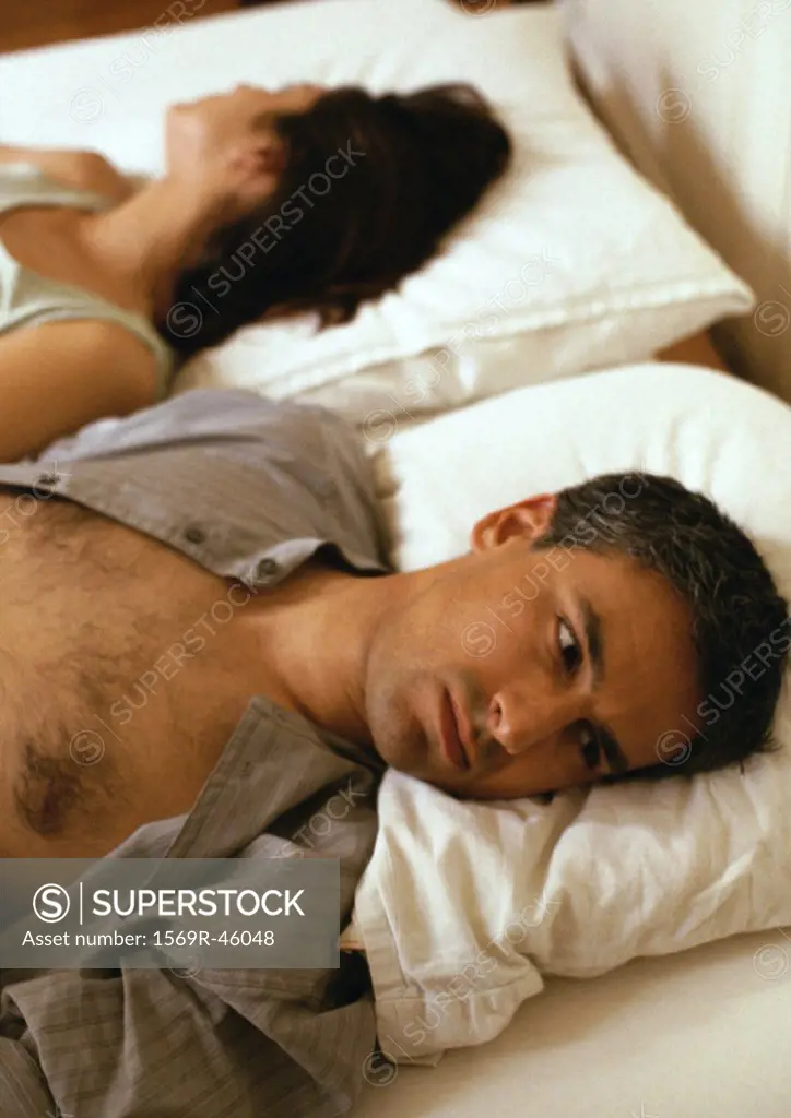 Man and woman lying in bed, heads on pillows, facing opposite directions, head and shoulders