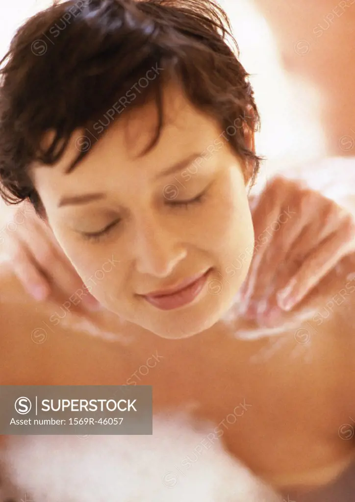 Woman in bubble bath with eyes closed, man´s hands massaging her shoulders, close-up
