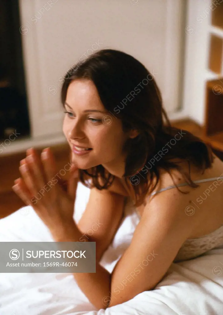 Woman propped up on elbows on bed with hands together, close-up, blurred motion