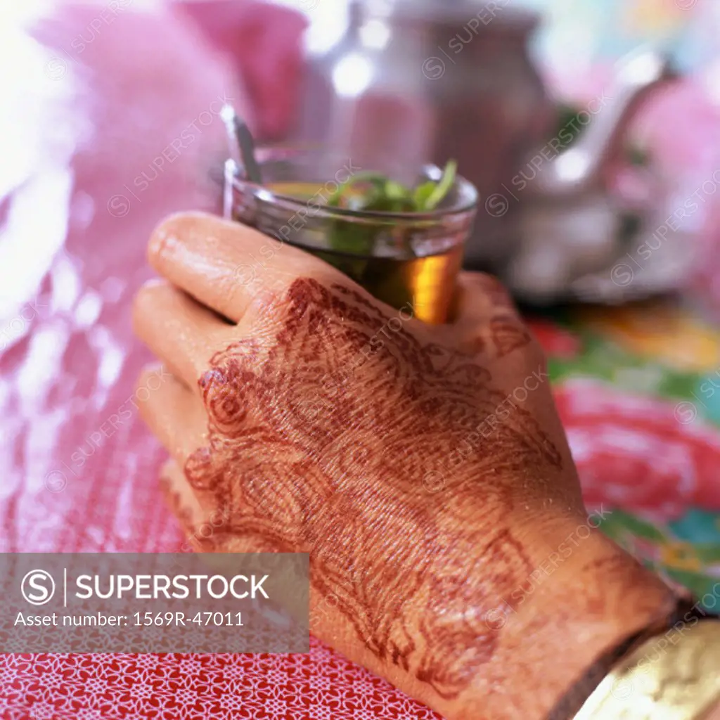 Hand with henna motif holding glass of mint tea, close-up
