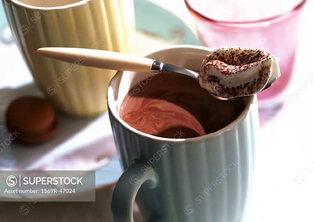 Hot chocolate in mugs with spoonfull of whipped cream, close-up