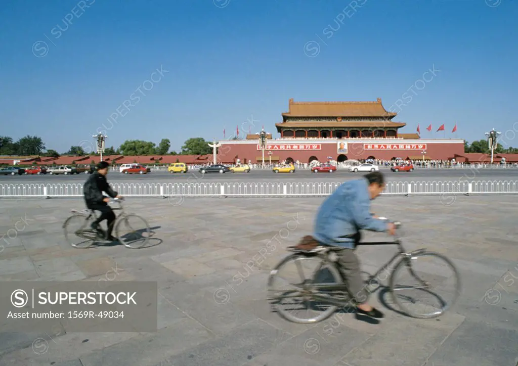 China, Beijing, two people riding bicycles in street in front of The Forbidden City