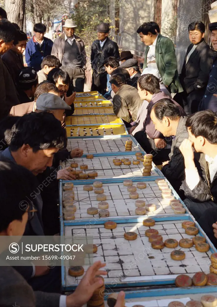 China, Xinjiang, Urumqi, line of people playing mah-jong outdoors