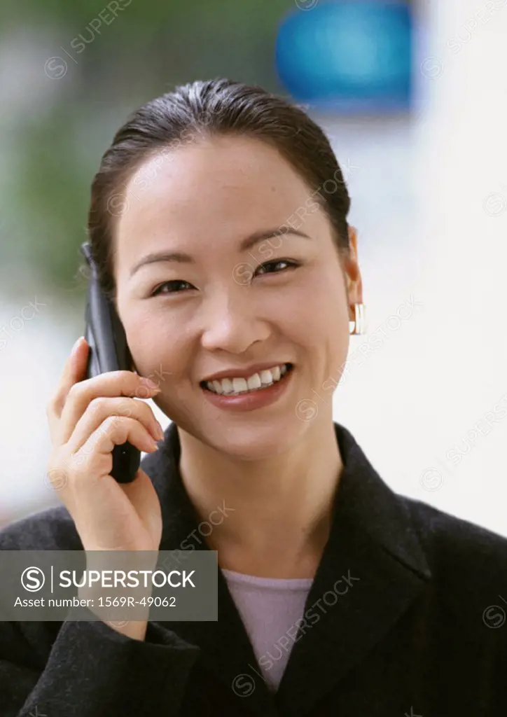 Woman using cell phone, smiling at camera, portrait