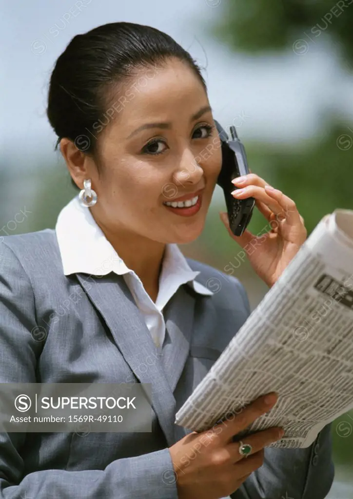 Woman using cell phone and holding newspaper, portrait