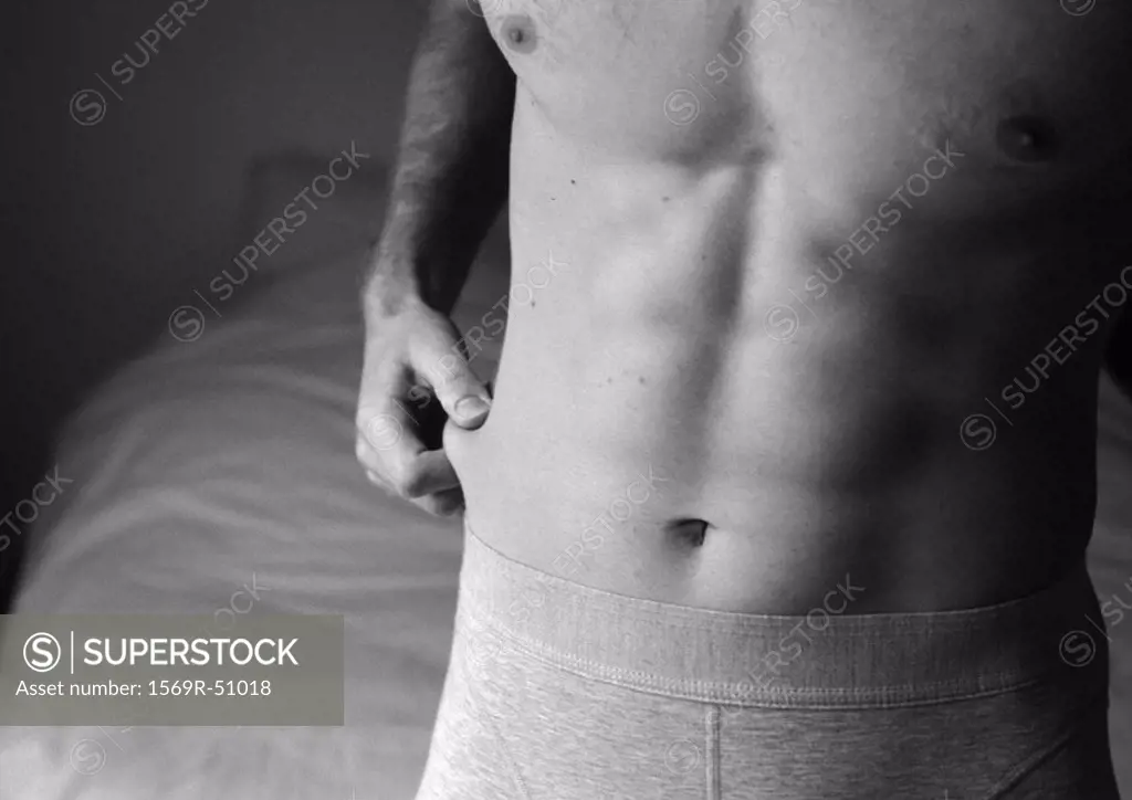 Man in underwear pinching waist, mid section, close-up, b&w