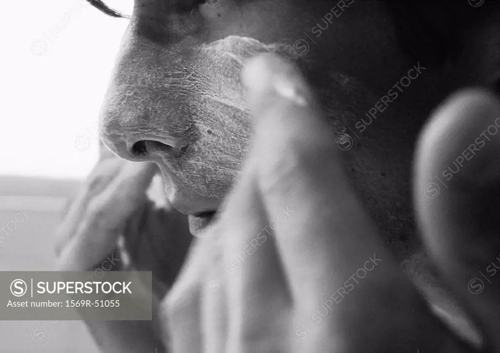 Man putting cream on face, close-up, b&w