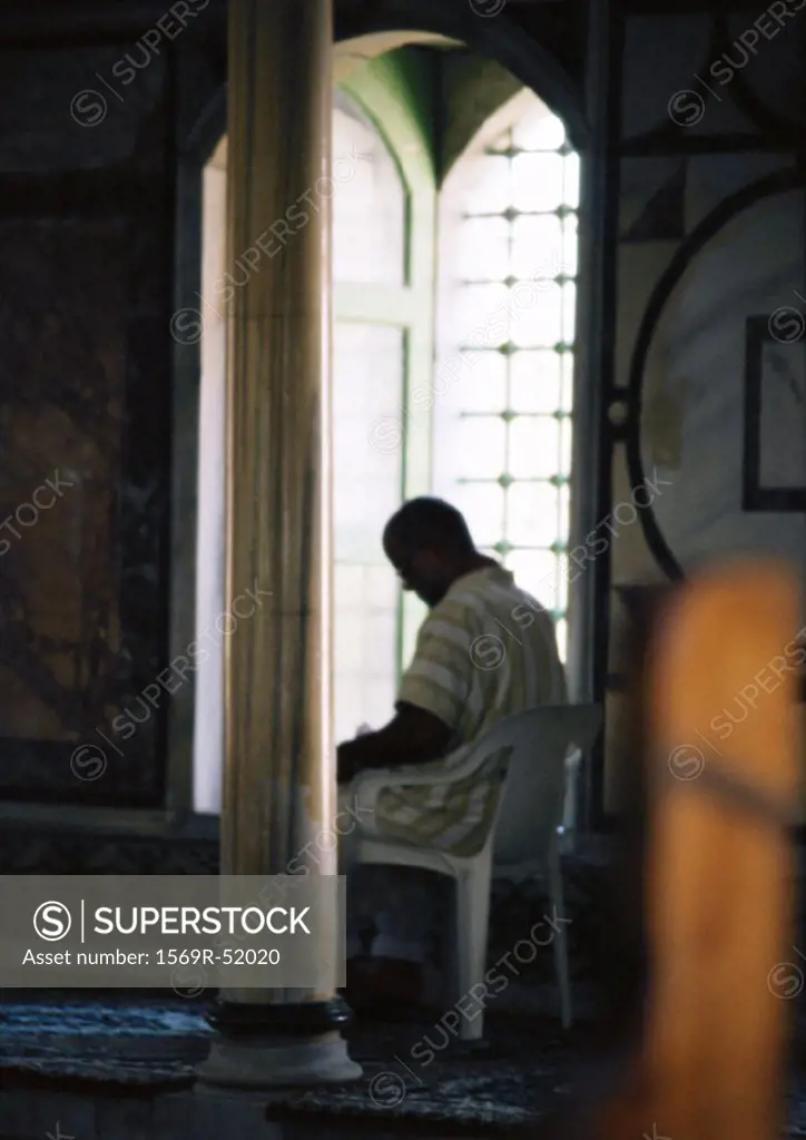 Israel, Jerusalem, person sitting in plastic chair in mosque, next to window