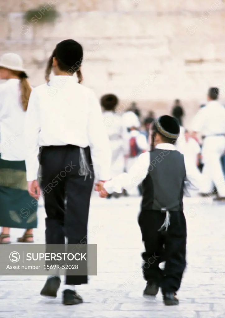 Israel, Jerusalem, two Orthodox Jewish boys wearing kippas and holding hands, rear view