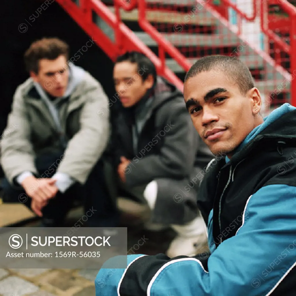 Focus on young man looking into camera in foreground, two young men squatting in background