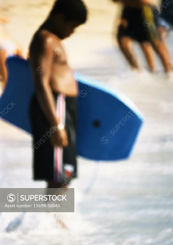 Person holding bodyboard, feet in water, blurred
