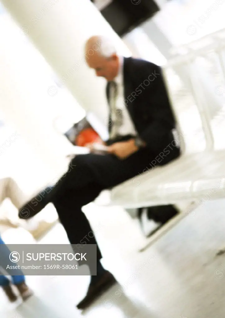 Mature man sitting on bench, reading, blurred