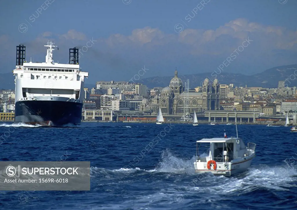 Ferry next to smaller moving boat, coastal city in background